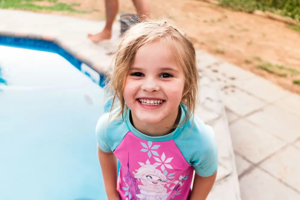 A child in a wetsuit and swim hat during a one-to-one swimming lesson in an unheated outdoor pool
