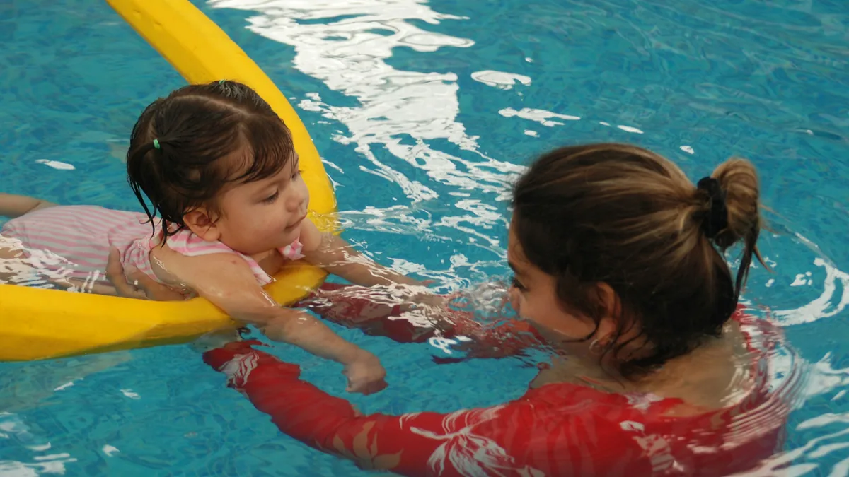 A swimming coach in the water supporting a young child one-to-one
